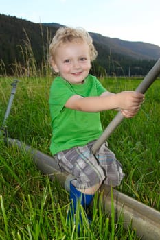Beautiful blond boy sitting in the field on the irrigation pipes.
