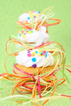 Three decorated vanilla cupcakes on a green background