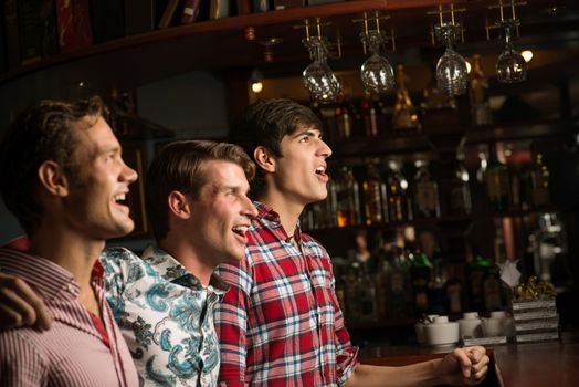 Three men stand in a row embracing smile and look in front of you, sports fans