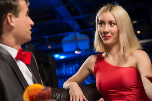 portrait of a woman in a nightclub, sitting on the couch and talking with man