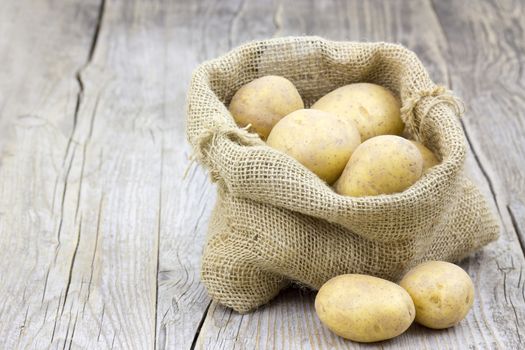 Raw potatoes in burlap bag on wooden background