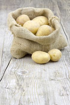 Raw potatoes in burlap bag on wooden background 