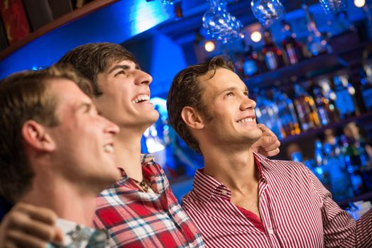 Three men stand in a row embracing smile and look in front of you, sports fans