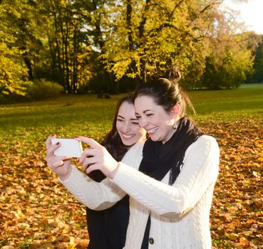laughing girlfriends with smartphone  in autumn park