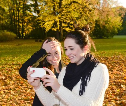 cheerful sisters with smartphone  in autumn park