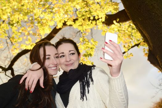 happy sisters with smartphone  in autumn park