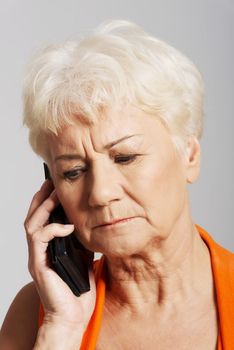 An old lady talking through phone.She is receiving bad news. Over grey background.