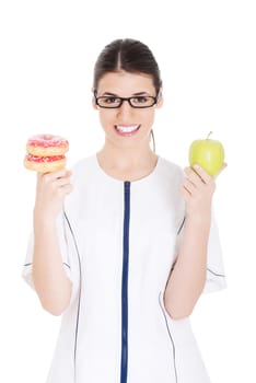 Young female doctor, nurse holding an apple and doughtnuts. Isolated on white.