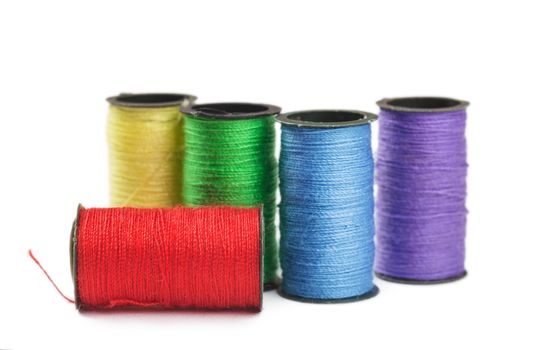 Five spools with green, red, yellow, violet and blue threads over white background