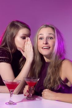 Female friends enjoying a night out sitting having cocktails at a table in a nightclub