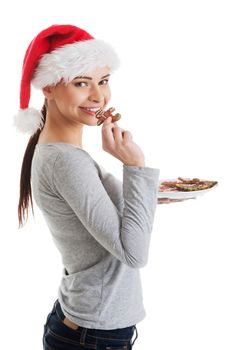 Beautiful woman in santa hat eating a cookie. Isolated on white.