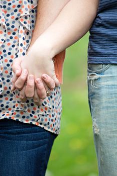 Close up of a young happy couple holding hands together at waist height.