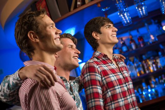 Three men stand in a row embracing smile and look in front of you, sports fans