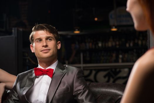 portrait of a man in a nightclub, sitting on the couch and talking with the woman, a date at a nightclub.