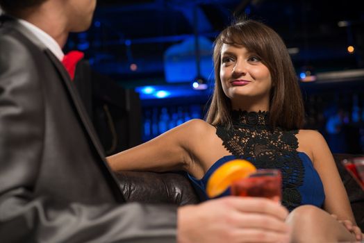 portrait of a woman in a nightclub, sitting on the couch and talking with man