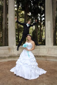A handsome groom playfully jumps on his bride from behind outdoors.