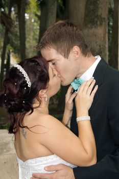 A handsome groom kisses his beautiful bride outdoors.