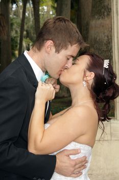 A handsome groom kisses his beautiful bride outdoors.