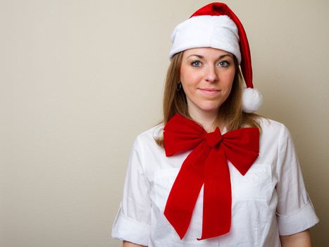 Woman with a santa hat smiles at the camera while wearing a bow