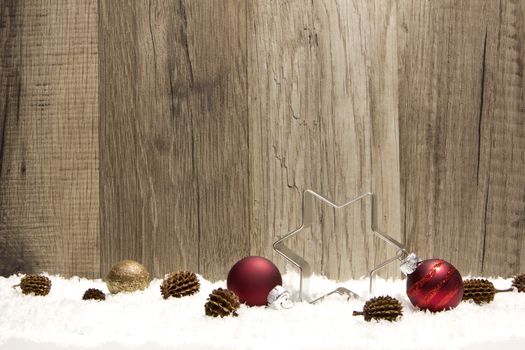 christmas decoration with wooden background, snow, christmas baubles red, poinsettia, and pine cones 