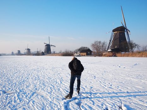 Person having fun while ice skating on a frozen canal along windmills at the Unesco World Heritage Site Kinderdijk in the Netherlands in winter.
