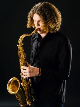 Photo of a teenager playing the saxophone over dark background.