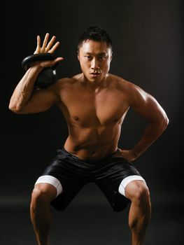 Photo of a muscular Asian man doing squats while holding a kettlebell.
