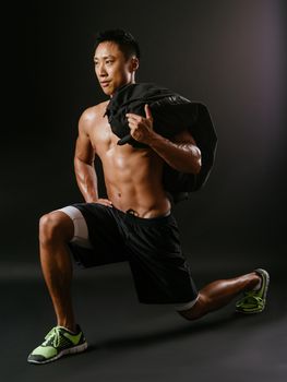 Photo of a muscular man doing lunges with a sand bag.