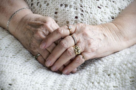 Senior woman hands crossed on her legs: loneliness or health issues.