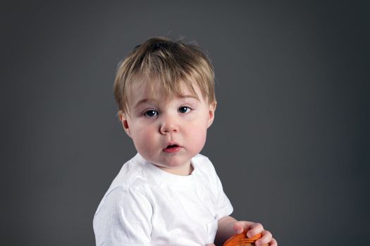 Portrait of little blond boy or toddler looking upset, desaturated on grey background.
