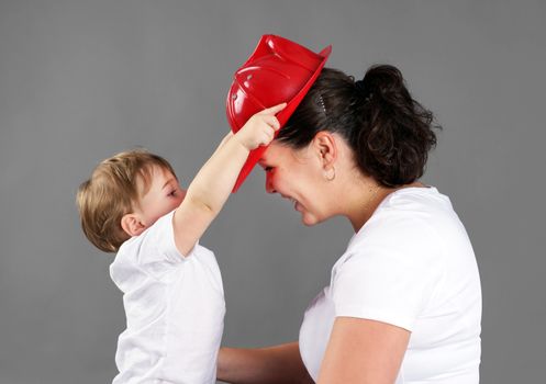 Mother and child playing, little blond boy or toddler putting a red plastic fireman's hat on mom