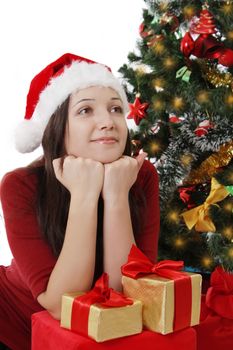 Dreaming Santa girl with gifts sitting under Christmas tree