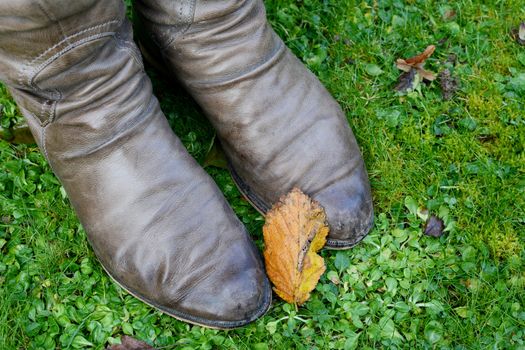 Golden autumn leaf rests on a woman's winter boots on green grass