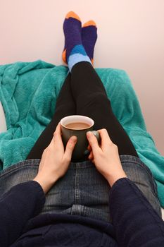 Woman holding a cup of coffee or tea, relaxing on the couch with her feet up