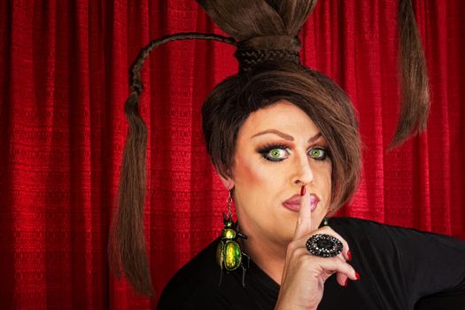 Man in drag and funny hairdo with finger near lips