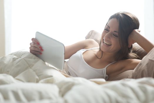Woman enjoying with a digital tablet in bed in the morning, waking up.