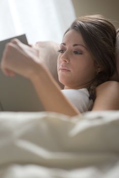 Woman lying in bed while reading a book 