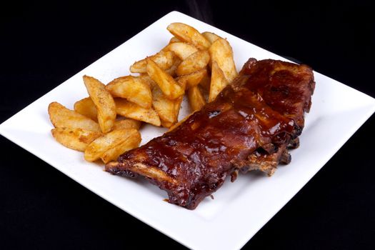 BBQ ribs with potato wedges on a white plate.