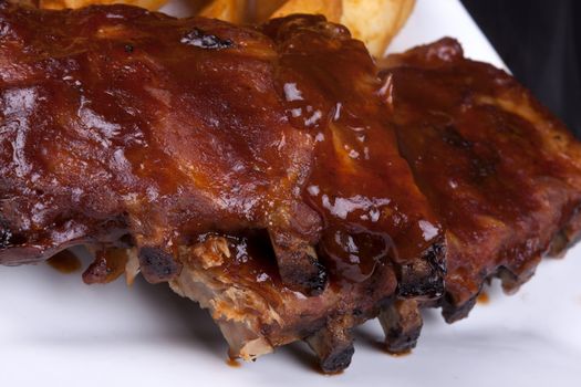 Close up BBQ ribs with potato wedges on a white plate.