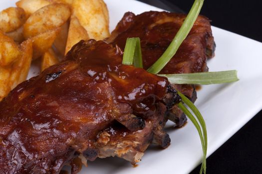 Close up BBQ ribs with potato wedges on a white plate.