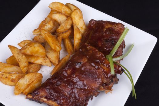 BBQ ribs with potato wedges on a white plate.