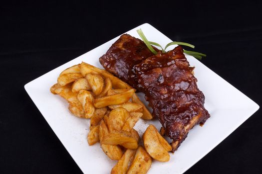 BBQ ribs with potato wedges on a white plate.