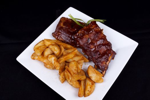 BBQ ribs with potato wedges on a white plate.