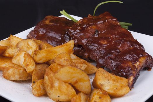 Close up BBQ ribs with potato wedges on a white plate.