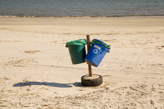 Blue and green plastic recycle bins on an empty beach in winter
