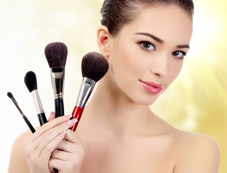 Pretty woman with cosmetic brushes against an abstract blurred background