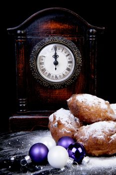 Dutch donut also known as oliebollen, traditional New Year's eve food, clock on midnight over black background