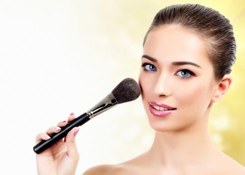 Pretty woman with cosmetic brushes against an abstract blurred background