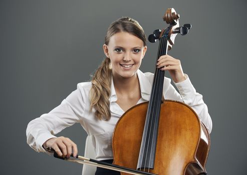 Smiling young woman cellist on grey background