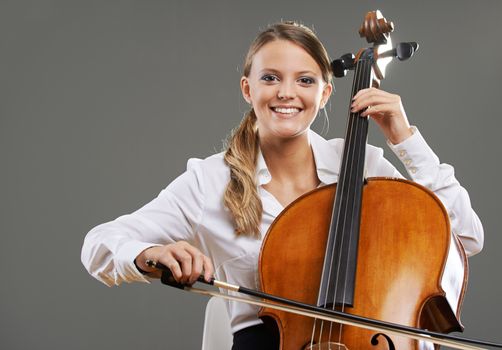 Smiling young woman cellist on grey background